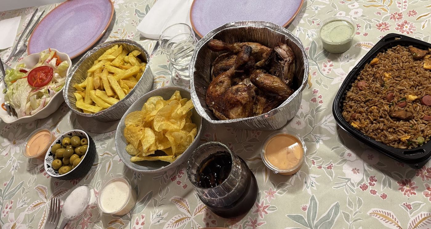 Mesa preparada con pollo asado, patatas, arroz chaufa y acompañamientos para compartir.